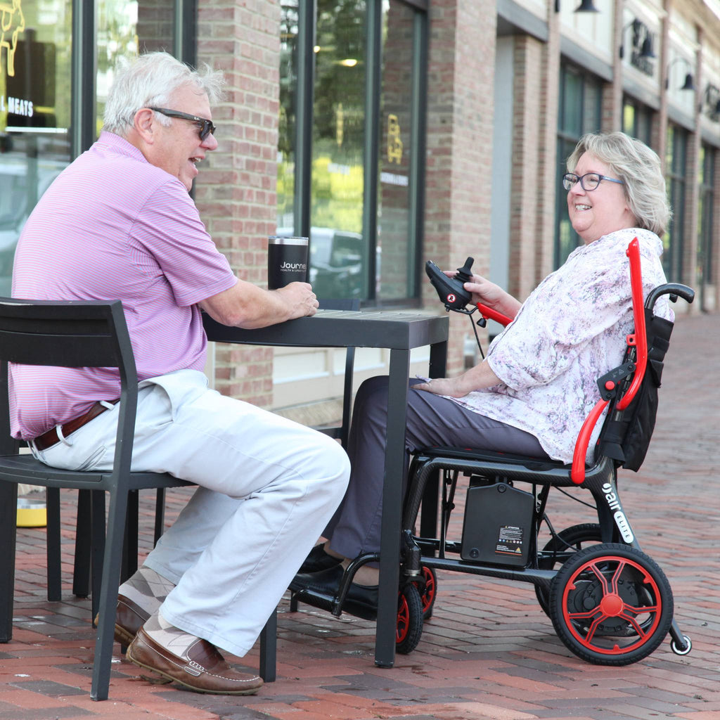 Woman seated in a Journey Air Elite power chair pulled up to an outdoor cafe table with a companion